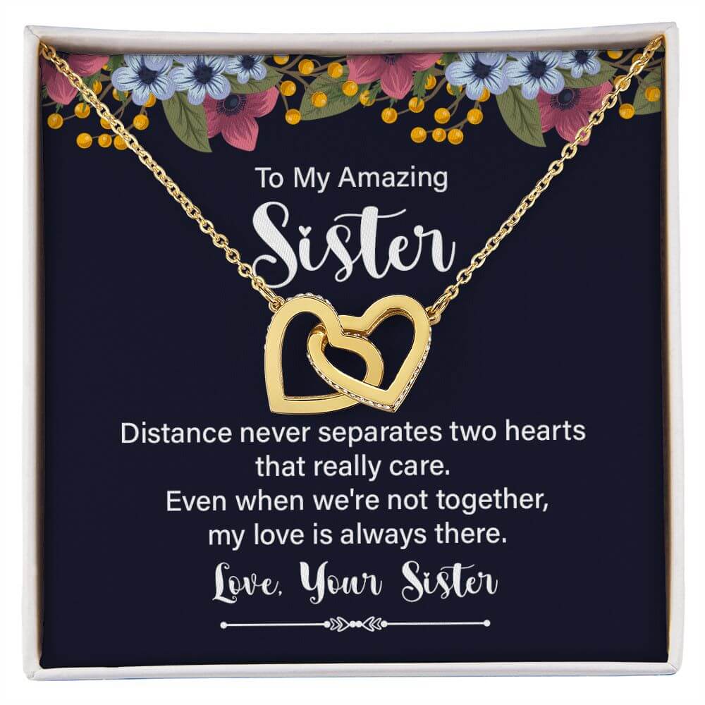 Amazing Sister yellow gold interlocking hearts necklace in open white gift box on rustic wood surface with dried flowers